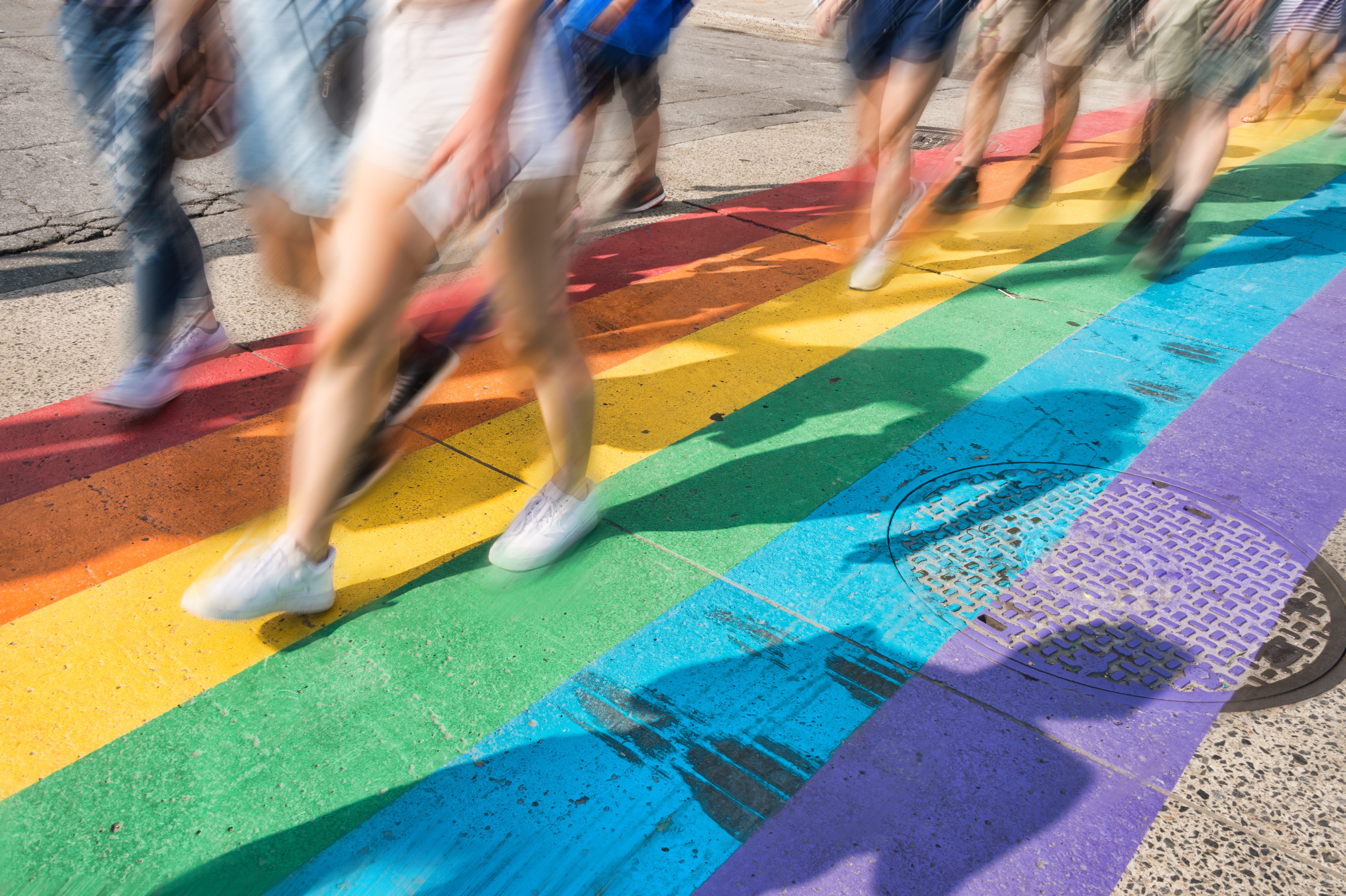 Camera focused downward to rainbow painted pedestrian crossing with people crossing