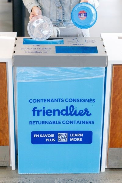 A person placing the Friendlier reusable container into the Friendlier blue bin.