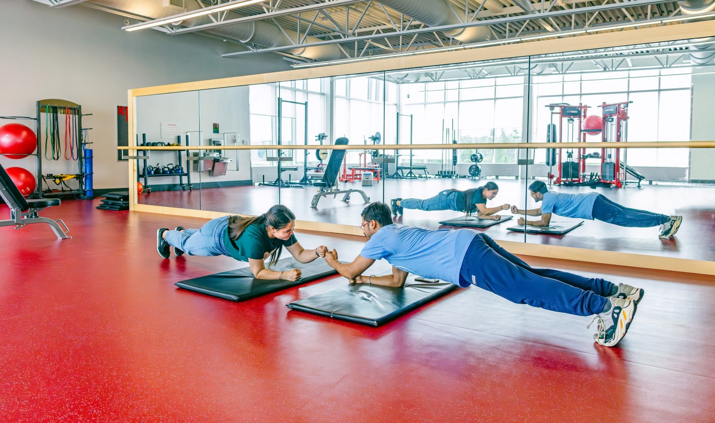 Two people perform a plank exercise together on the floor in one of Seneca's fitness centres.