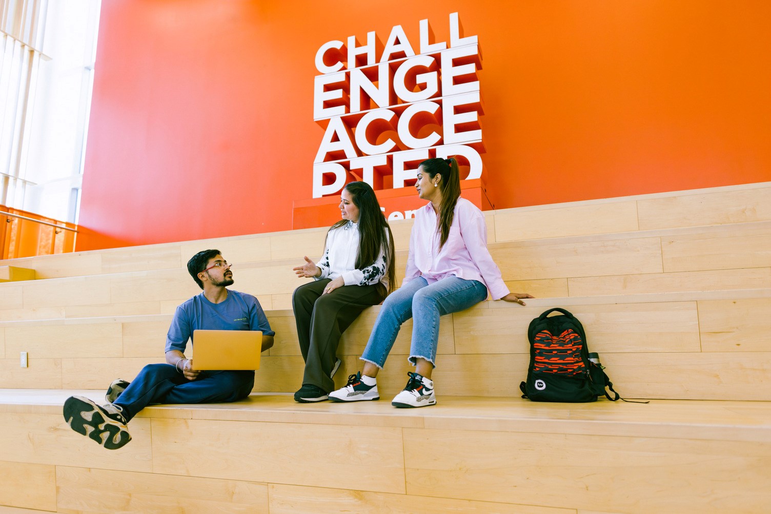 Three people sit on amphitheatre-style seating while holding an animated conversation.