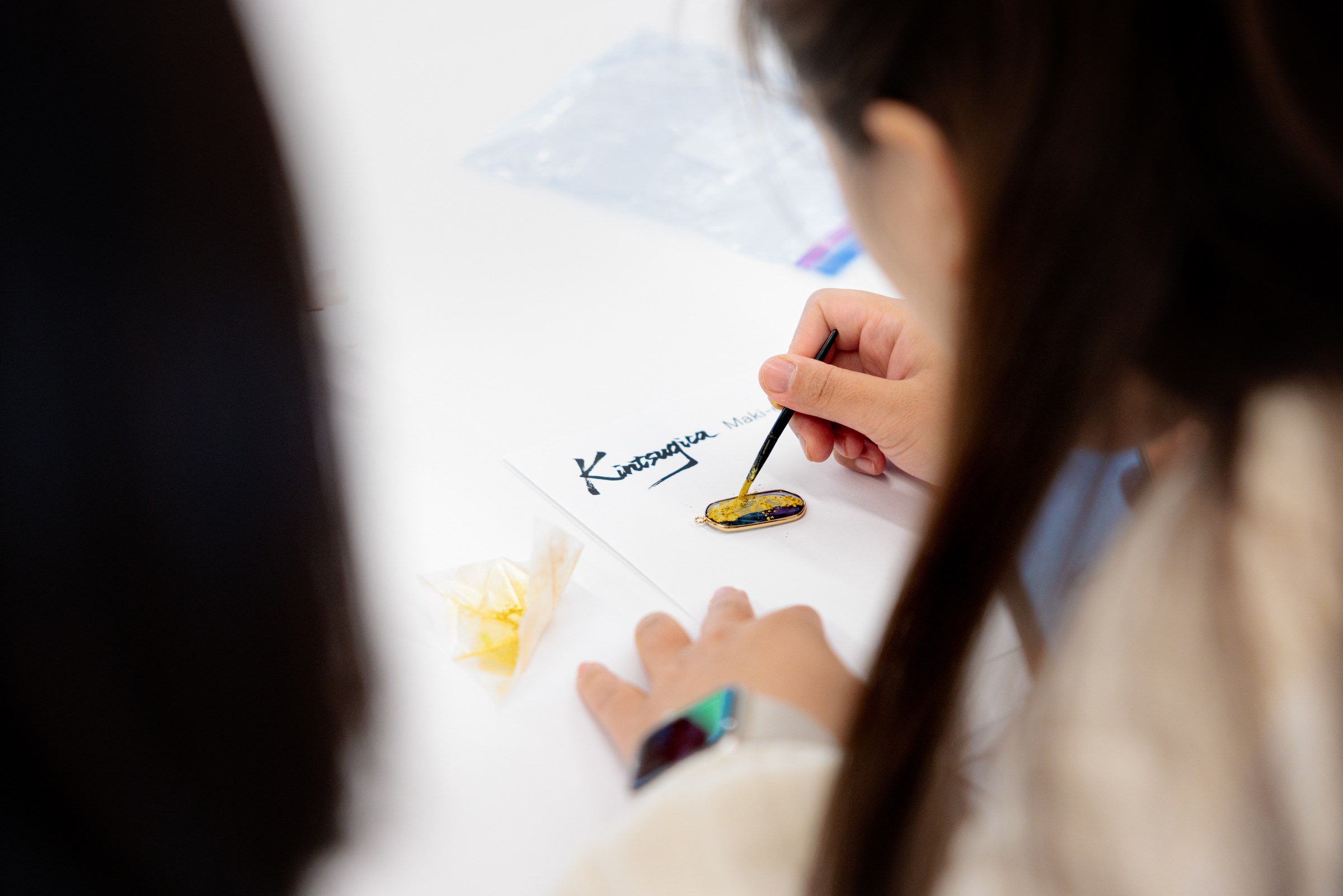 A student applying gold powder to their Maki-e piece